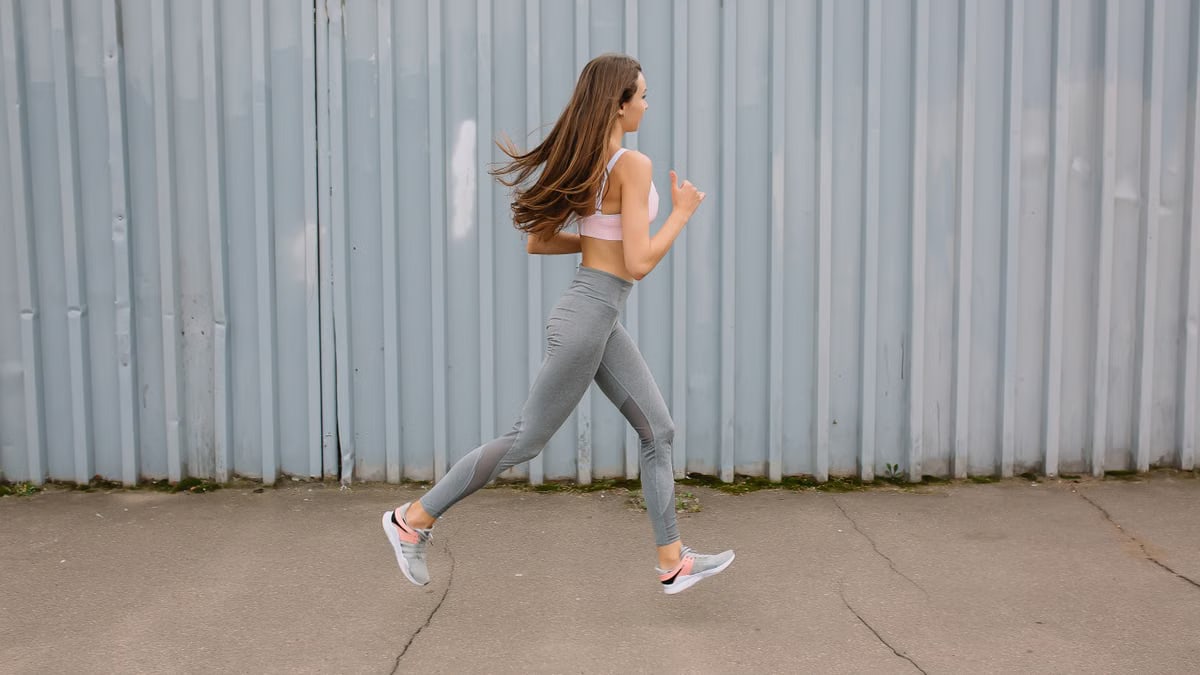 Fit woman running outdoors in activewear with sports bra and leggings. Motion captured at day time.